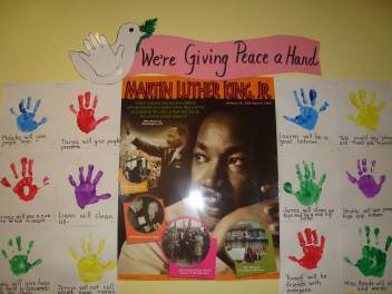 A MLK display board. Different color hand prints on paper next to a Martin Luther King poster. Heading reads We're Giving Peace a Hand. 