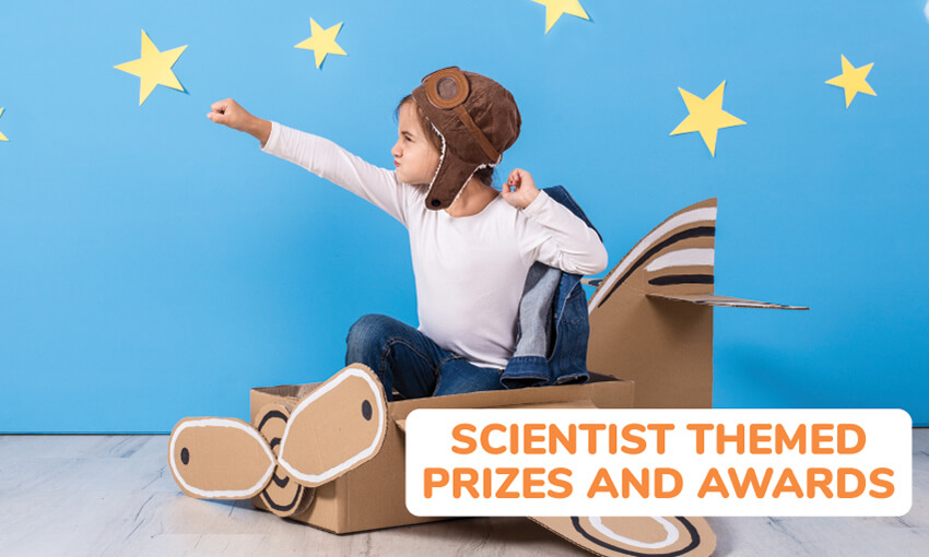 A picture of a kid in a cardboard airplane with one arm and fist outstretched in front of him. He's wearing an old airplane helmet and goggles in front a blue background with yellow stars on the background. Text reads scientist themed prizes and awards. 