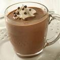 A picture of hot chocolate with whipped cream and chocolate chunks on the whipped cream. In a glass see through mug. 