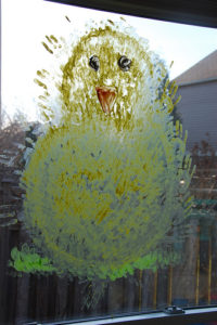 A picture of a yellow baby chick painted on glass. 