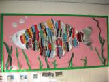 A picture of a fish art project on a school wall. The fish was made from plates that had been individually woven on by kids.
