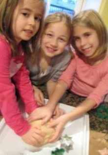 Three young girls kneading the gingerbread playdough. 