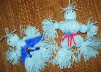 A picture of two yarn doll crafts with a wooden background. 