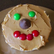 A rice cake with peanut butter spread on top. A hershey's kiss in place of it's nose, red M&Ms as the mouth, and green M&Ms as the eyes. 