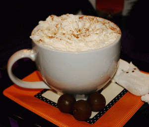 A picture of pumpkin spice hot cocoa in a mug with whipped cream on top sitting on a red and white plate. 