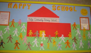 A bulletin board with a red school on it with words that say Happy School. there are sever kids either painted or drawn around the red school. 