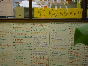 A white board with a list of different ways to be kind written on it. The heading of the whiteboard reads "180 Ways to Be Kind." 