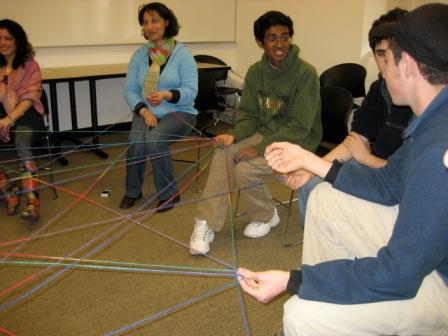 A picture of people sitting in a circle playing the spiderweb of friendship get to know you game. 