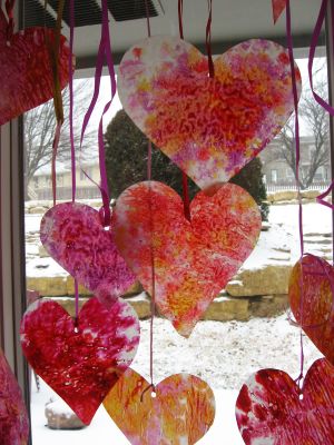 A picture of hearts dangling from red ribbon. The hearts are various colors and have a unique pattern to them. 