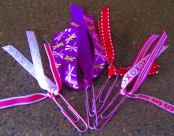 A picture of decorative paperclip bookmarks. The paperclips have lacy, pink, red, and purple strands coming from the paperclip. 