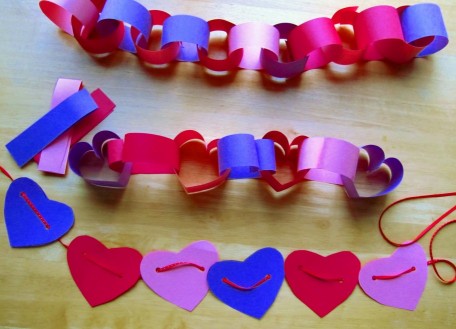 A picture of valentines construction paper chains. One has heart shapes. One has circular shapes. The other is just a string of heart cutouts. All in blue, purple, pink, and red construction paper colors. 