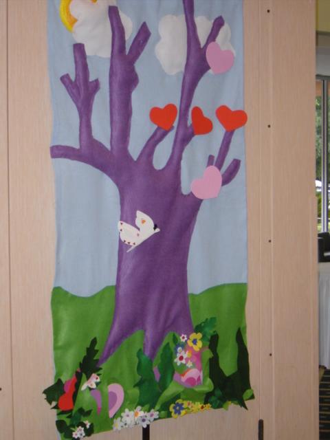 An image of art. The tree is purple, the leaves are red and pink hearts. There's grass and flowers around the base of the tree. 