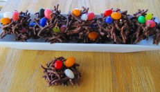 An image of a treat that looks like a birds nest. The chocolate looks like small twigs and in the center of each snack is 3 jelly beans representing eggs. 