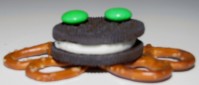 An Oreo with pretzels and green M&M's assembled to look like a frog. 