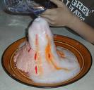 An image of a child pour vinegar into the volcano causing an eruption. The science experiment is on a tray to contain the overflowing lava.