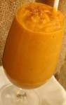 A picture of orange pumpkin smoothie in a tall see through glass with a straw. 