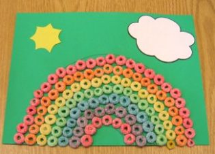 A picture of a fruit loops rainbow on green construction paper with a sun and cloud. 