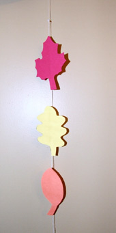A picture of a leaf mobile. A string of three leaf cutouts. A red one followed by a yellow then an orange one. 