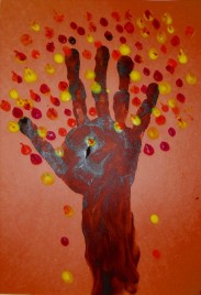 A arm and hand print on construction paper. The arm looks like the trunk of the tree and the fingers are the branches. Orange, yellow, and red paint dots for leaves.  