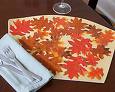 A fall themed placemat. This off white placemat has brown, orange, and red leaves cutout and pasted on it. 