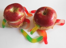 A picture of apples that were slice and had gummy worms inserted to have them coming out of the apple. Two apples with gummy worms. 