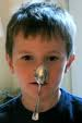 A kid balancing a spoon on his nose. 