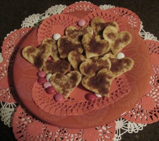 Heart shaped baked tortilla treats with cinnamon on top. On top of heart shaped paper doilies.