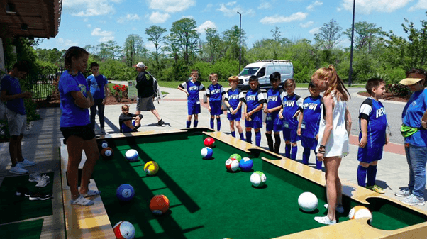a giant soccer billiard table/field where kids kick balls to pockets 