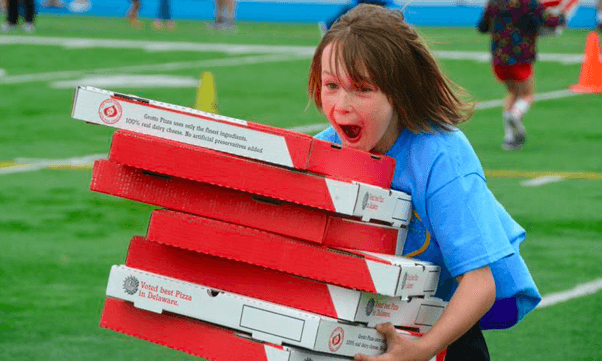 a kid carrying many boxes of pizzas 